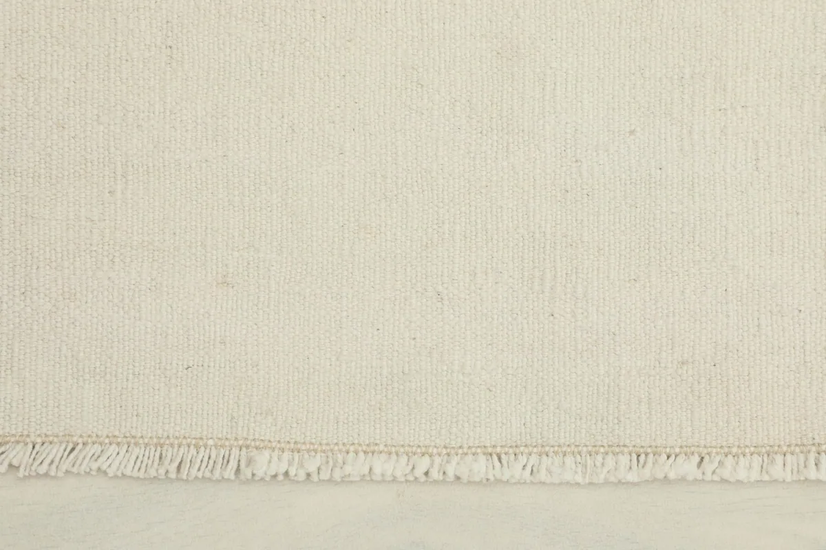 Close-up detail of the ivory wool pile and short fringes of the hand-knotted rug