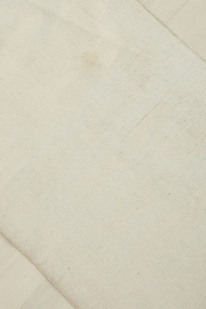 Detailed view of the rug's surface, showing subtle variations in the ivory wool and light patina