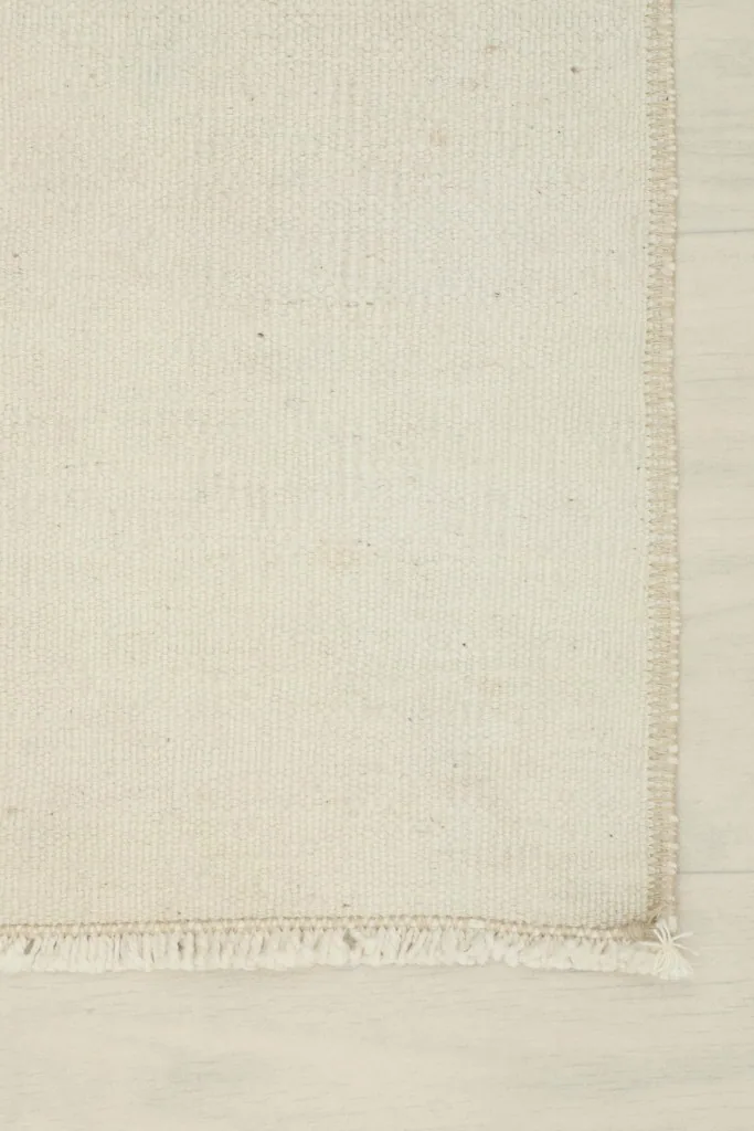 Corner detail showing the finished edge and short fringe of the hand-knotted ivory rug
