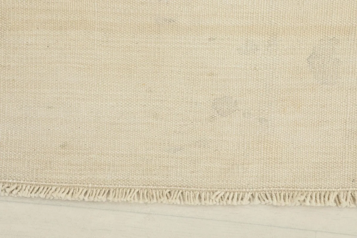 Close-up of the rug's short fringe and the low pile texture in ivory and beige tones.