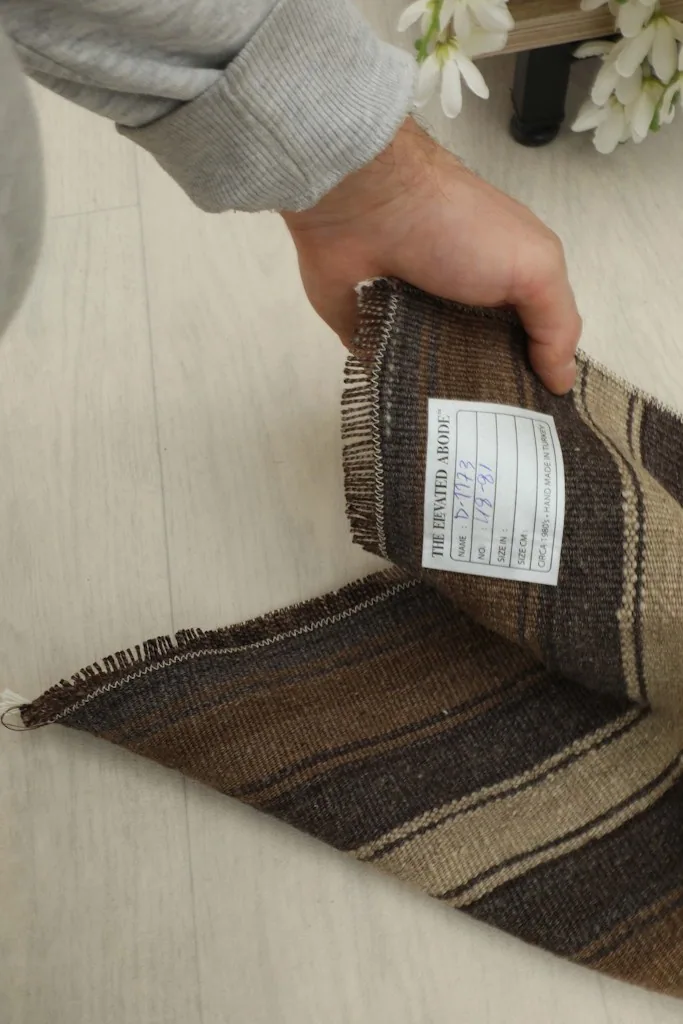 Hand holding a corner of the rug, showing the product label and the quality of the vintage textile