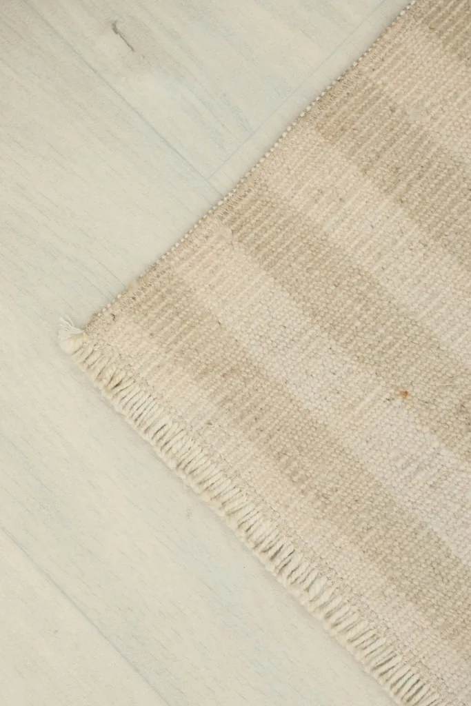 Diagonal view of the rug's striped texture and corner on a light wooden floor.