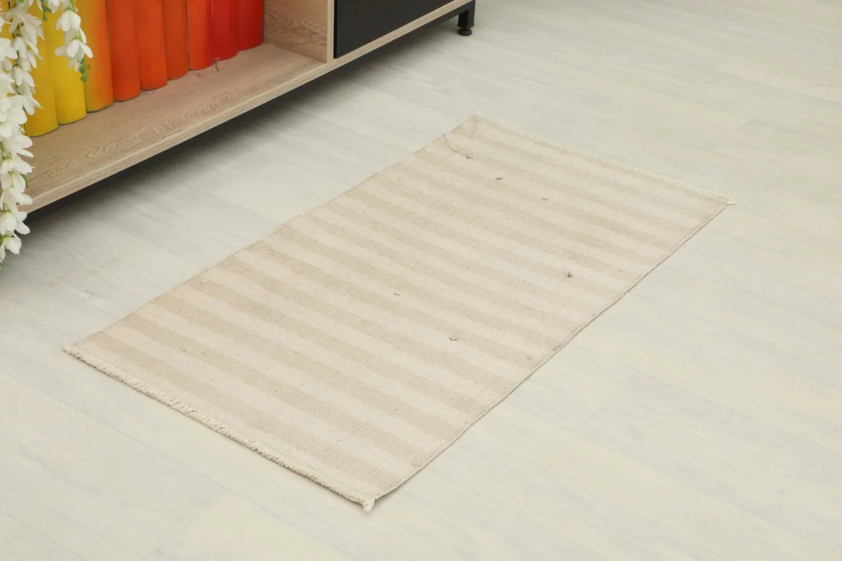 Angle view of the striped beige rug in a room setting next to a low shelf.