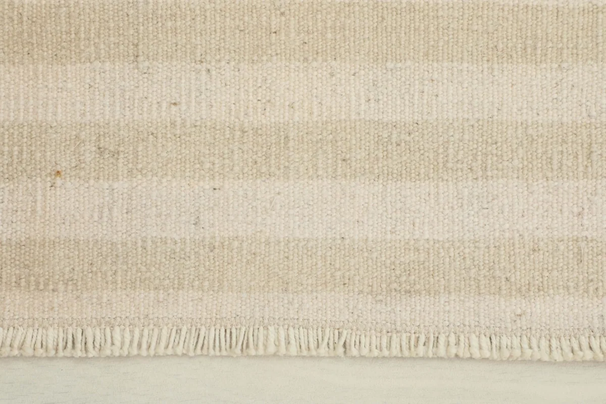 Close-up view of the beige and cream stripes and fringe detail of the rug.