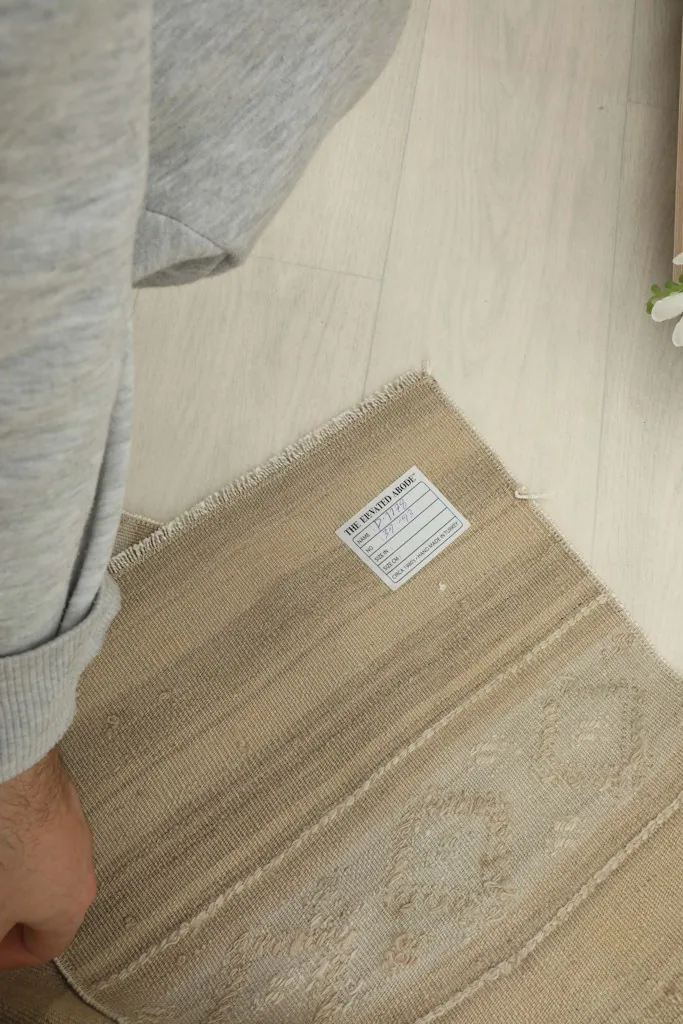 A hand holding the rug, revealing the label and texture of the vintage wool