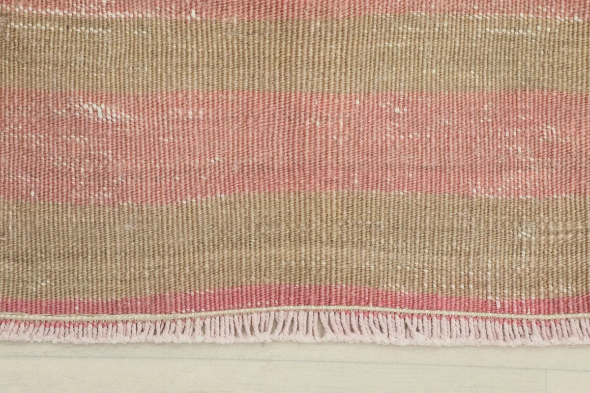 Close-up of the rug's short fringe and the texture of the pink and beige wool stripes.