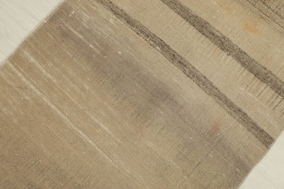 Detailed view of the distressed low pile and horizontal gray stripe on the tan rug