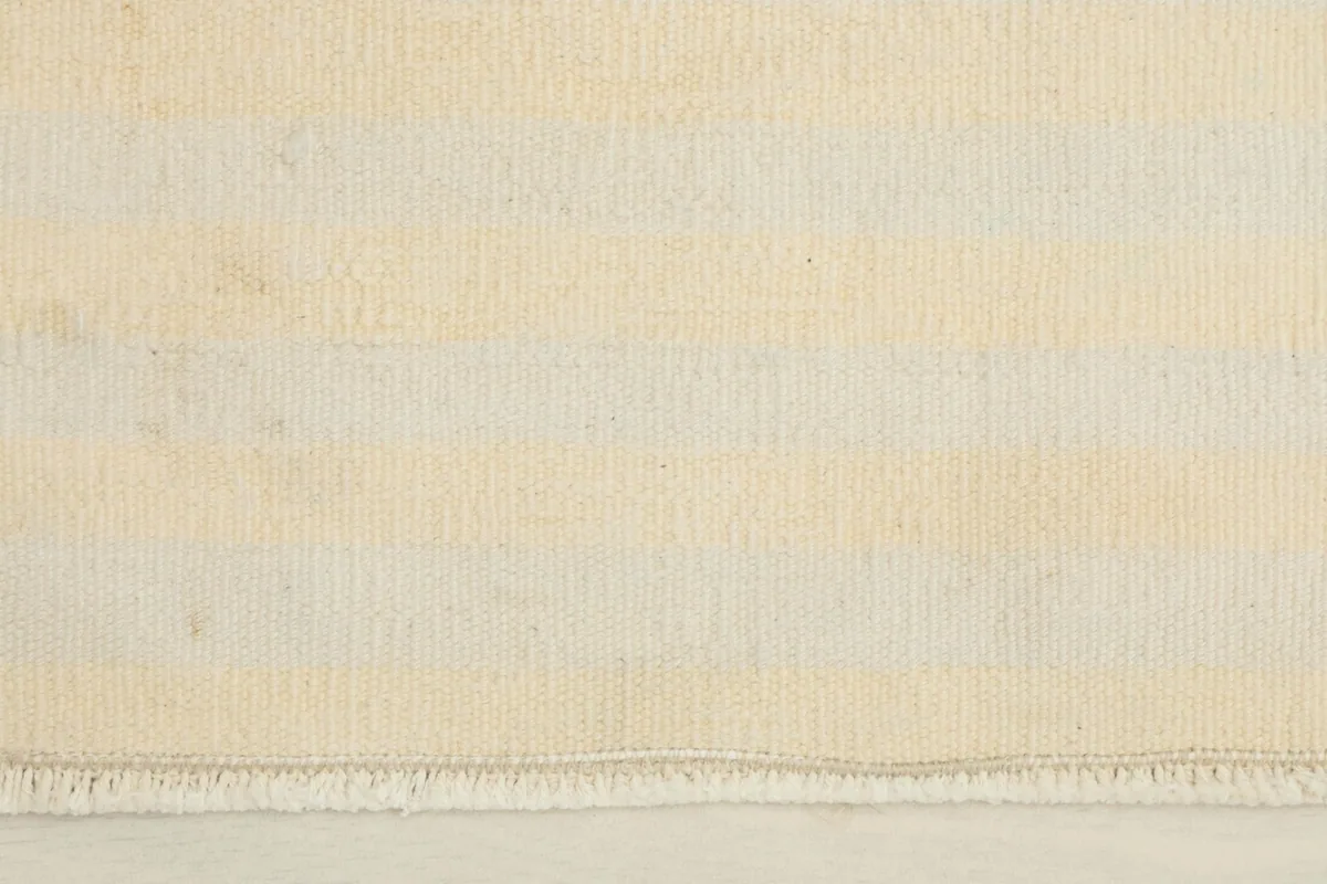Close-up detail of the horizontal ivory and beige stripes and the short fringe on one end of the rug.