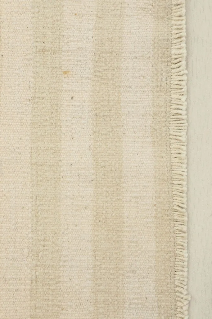 Close-up detail of the rug's beige and ivory stripes and fringe at one end.