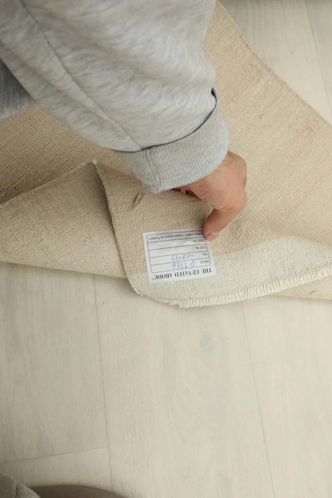Hand lifting the rug to reveal the back, showing the woven cotton foundation and label