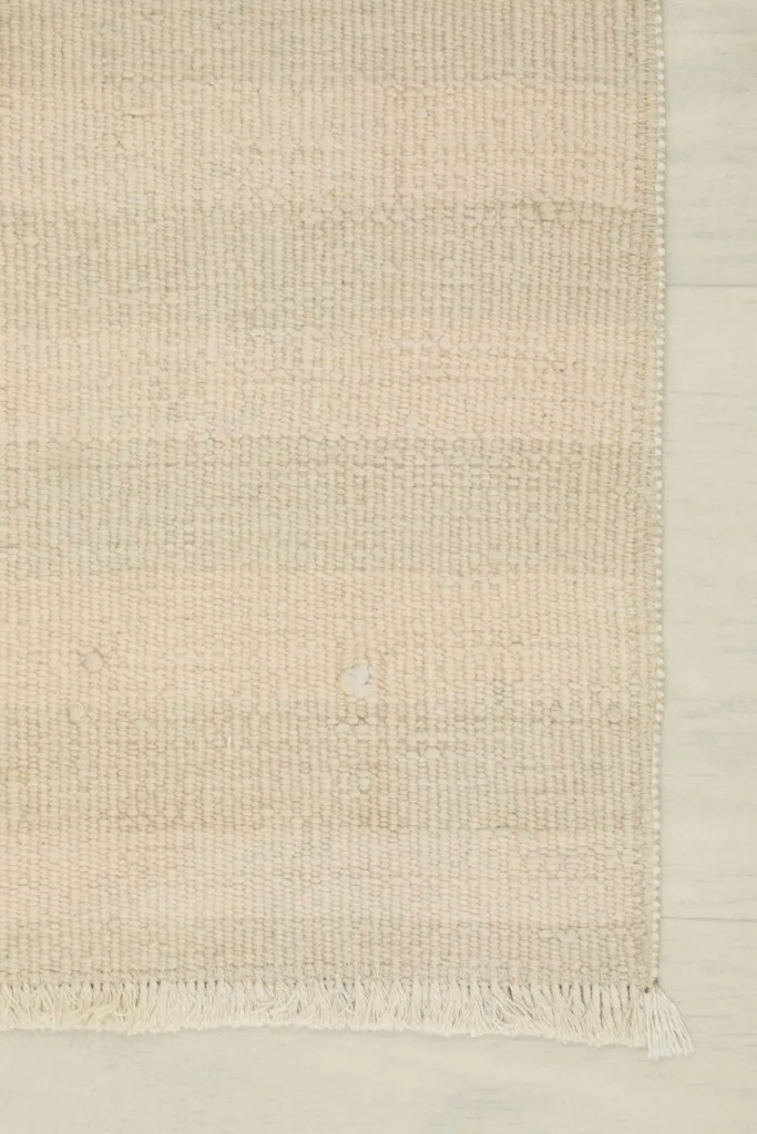 Edge detail of the ivory and cream rug, showing the fringe and side finishing.