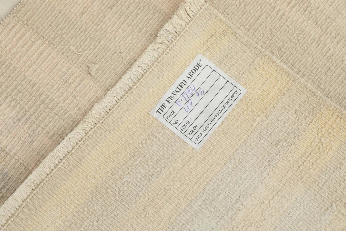 View of the back of the rug with a product label, showing the cotton foundation and knotting.