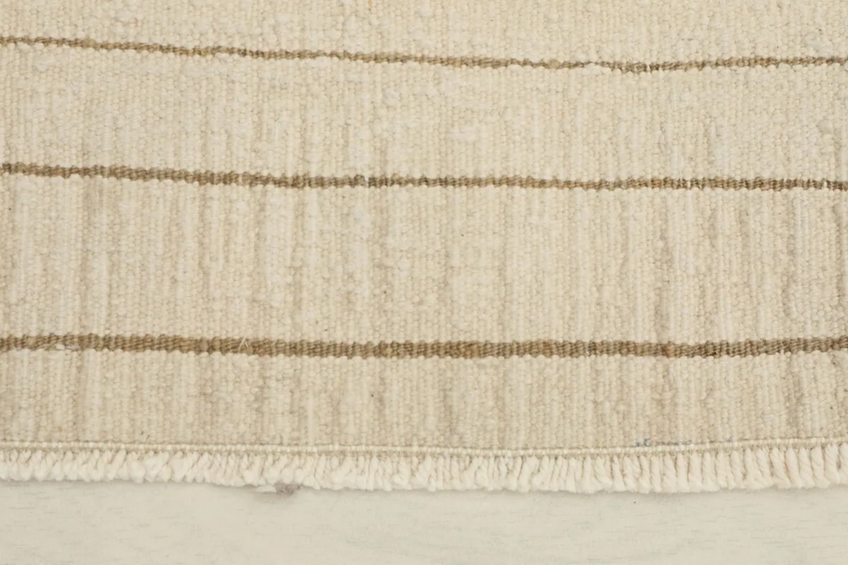 Close-up of the fringe and edge of the hand-knotted wool rug, highlighting the beige and brown stripes.