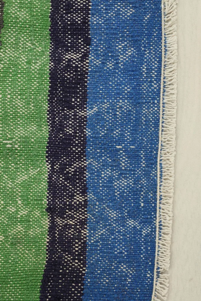 Close-up detail of the hand-knotted wool pile and cotton foundation, showing blue and green stripes.