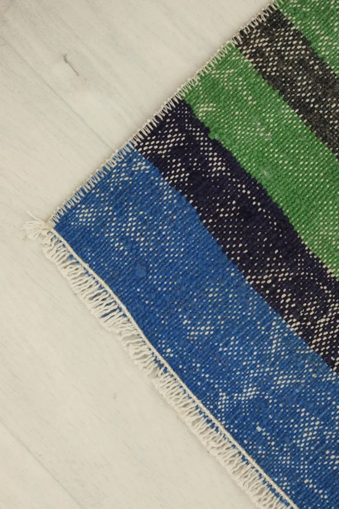 Corner detail of the rug, showing the fringe and the transition between blue and navy stripes.