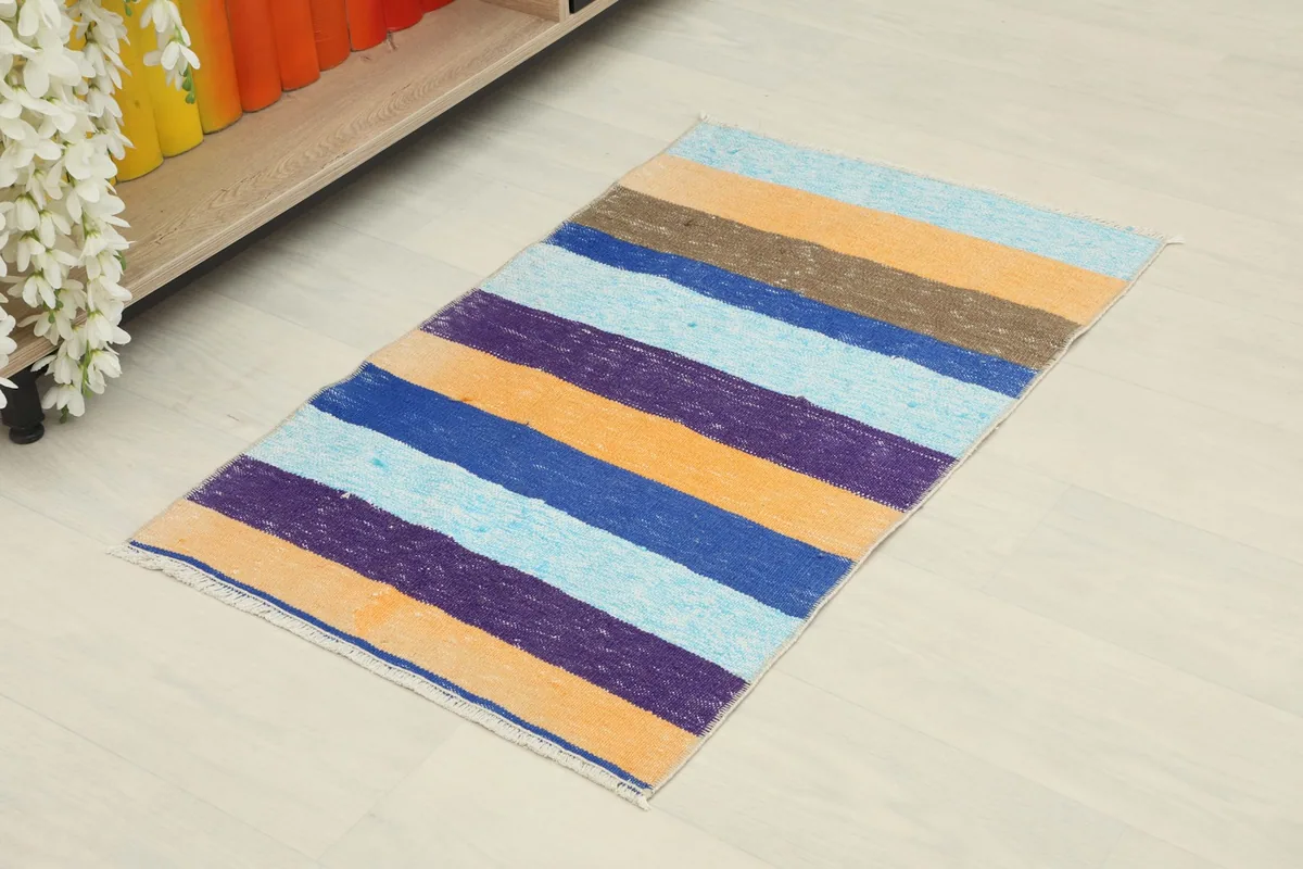 Angled view of the striped rug, showing its vibrant orange, blue, purple, and brown colors.