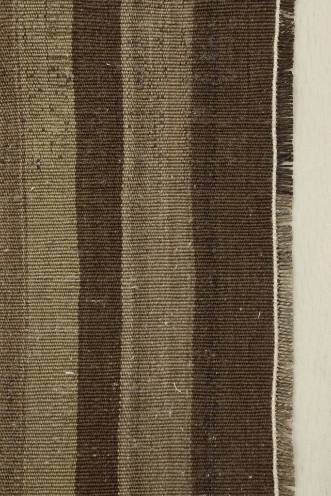 Close-up detail of the striped pattern and the natural fringe at one end of the vintage rug.