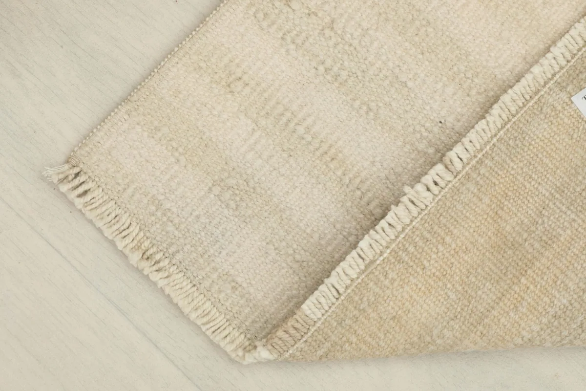 Partial view of the rug with a corner folded back, revealing the reverse side and foundation.