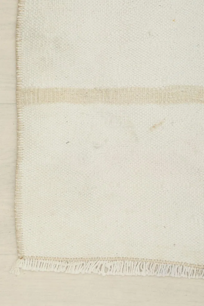 Detailed view of the corner of the rug, showing the cream wool pile, tan stripe, and finished edge.