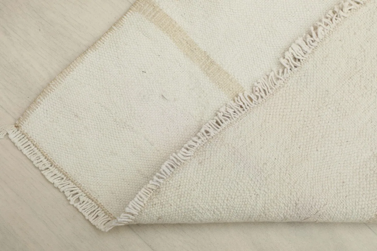 Partial view of the rug's underside and folded edge, showing the cotton foundation and knotting.