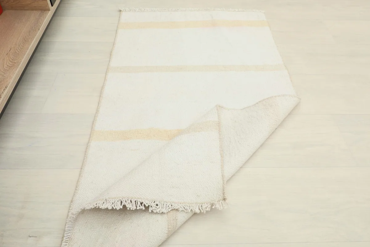 The rug partially folded, displaying its flexibility and the cream and tan striped pattern.