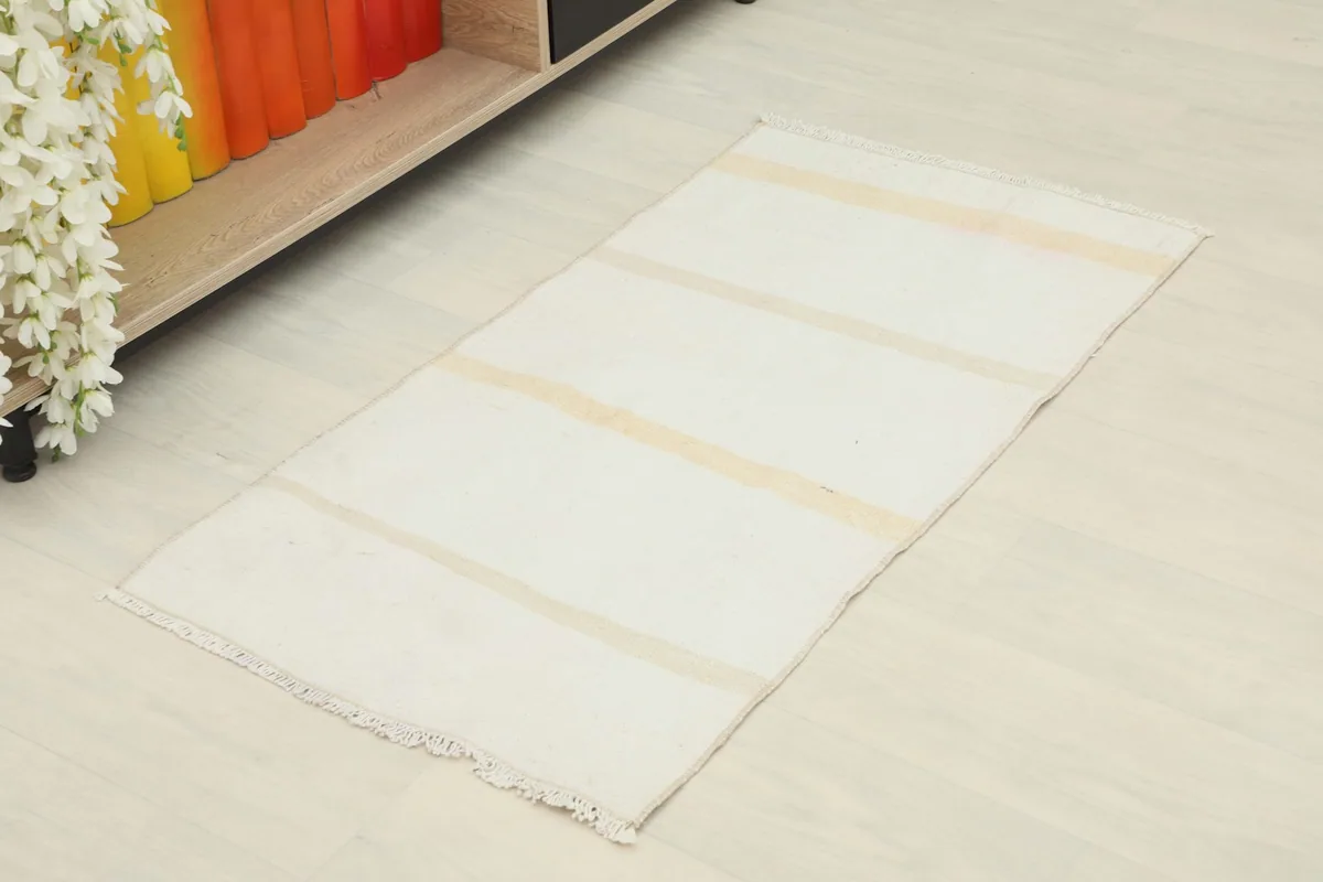 Slightly angled overhead view of the cream doormat rug, showing its rectangular shape and tan stripes.