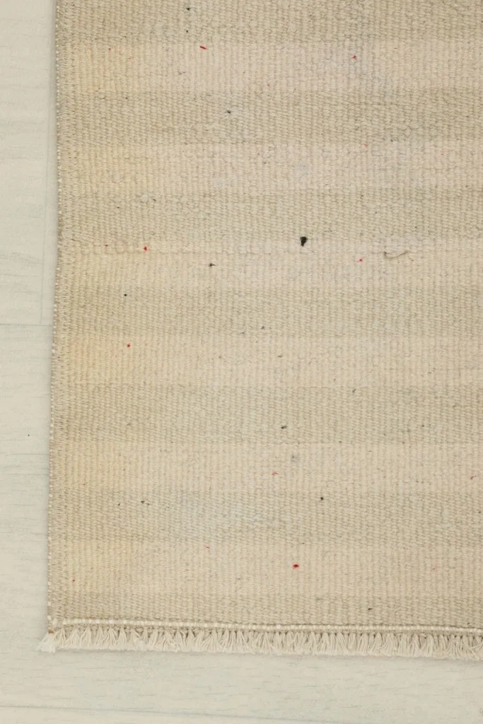 Close-up of one end of the rug, showing the beige stripes and the finished edge with minimal fringe.