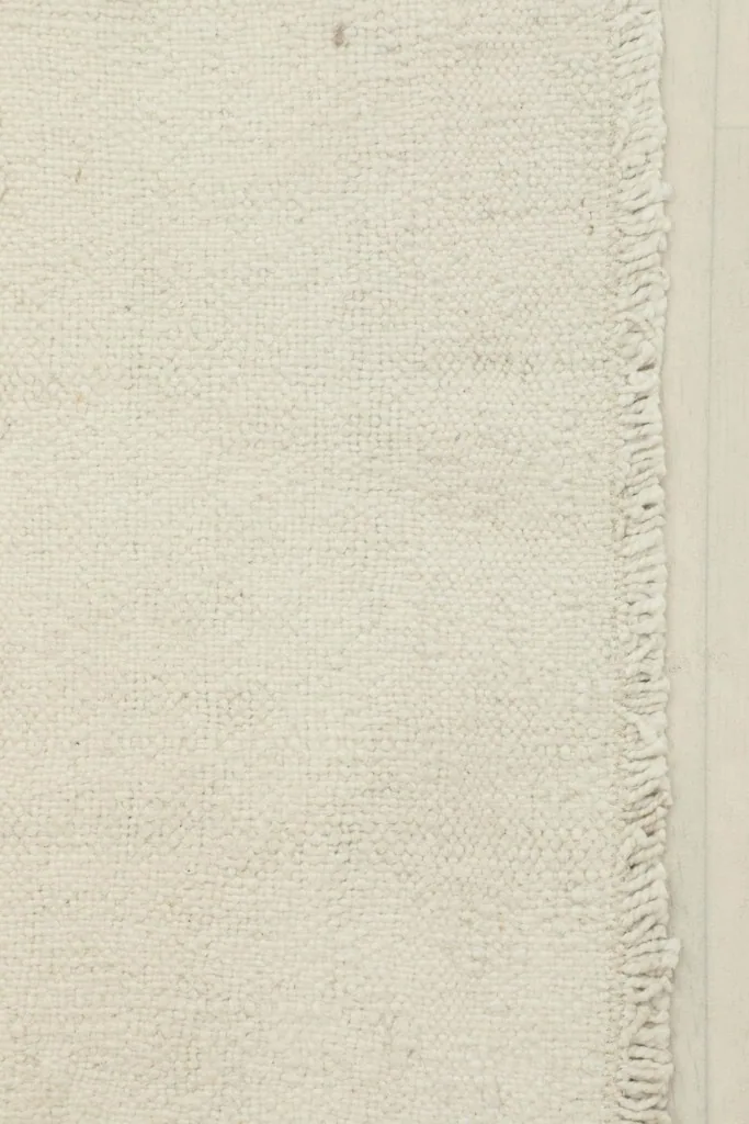 Close-up detail of the hand-knotted wool pile and fringe along one edge of the ivory rug