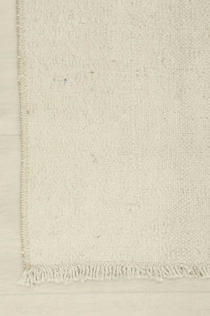 Corner detail of the ivory rug, highlighting the fringe and finished edge