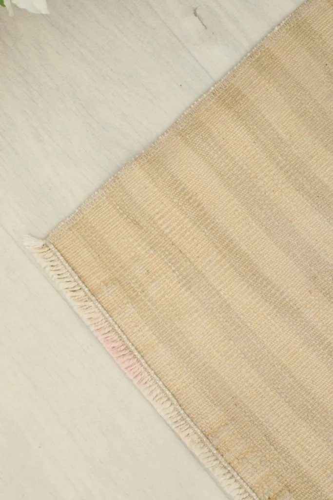 Angled view focusing on the corner and short fringe of the beige and tan striped rug.