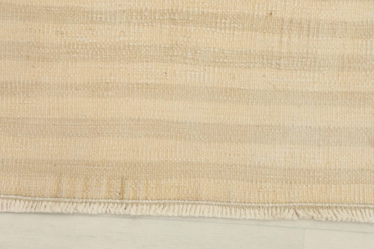 Close-up detail of the rug's low pile and fringed edge, showing the beige and tan striped texture.