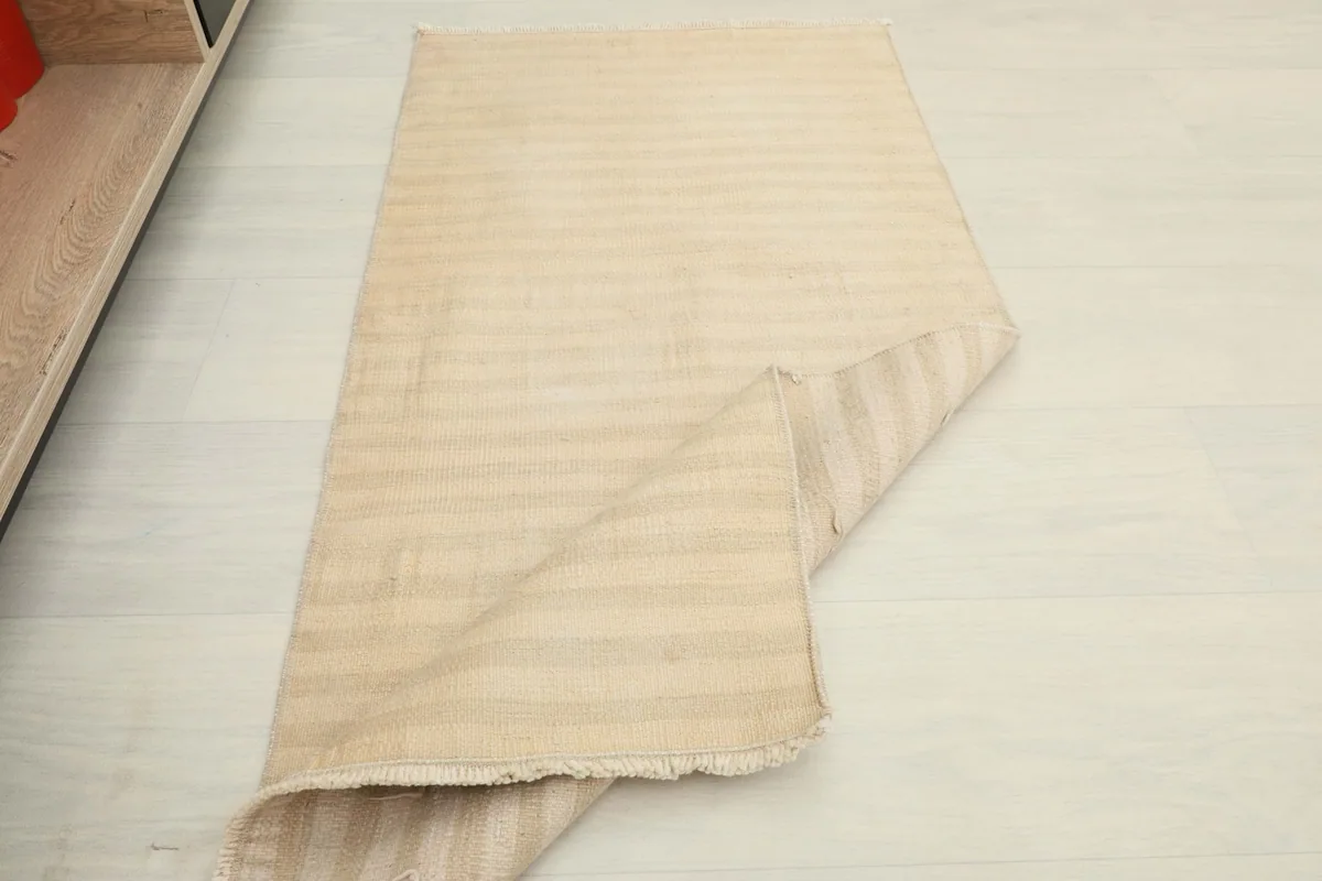 The beige striped rug partially folded, demonstrating its flexibility and texture.