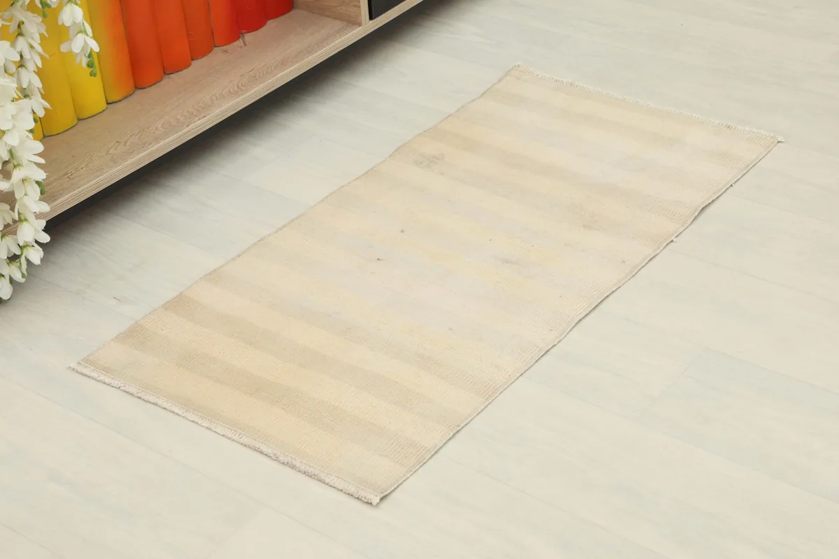 Angled view of the beige and cream striped doormat rug, highlighting its rectangular shape and subtle color variations.