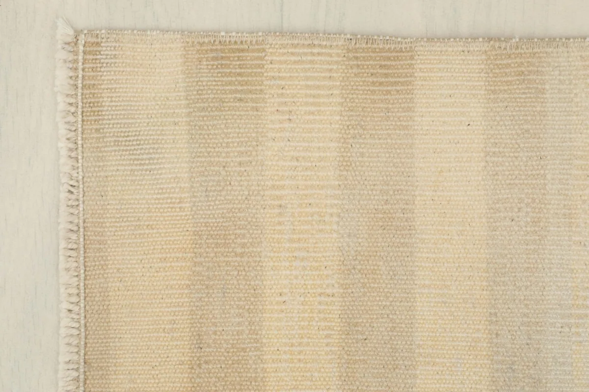 Corner detail of the beige striped rug, showcasing the tight weave and short fringe.