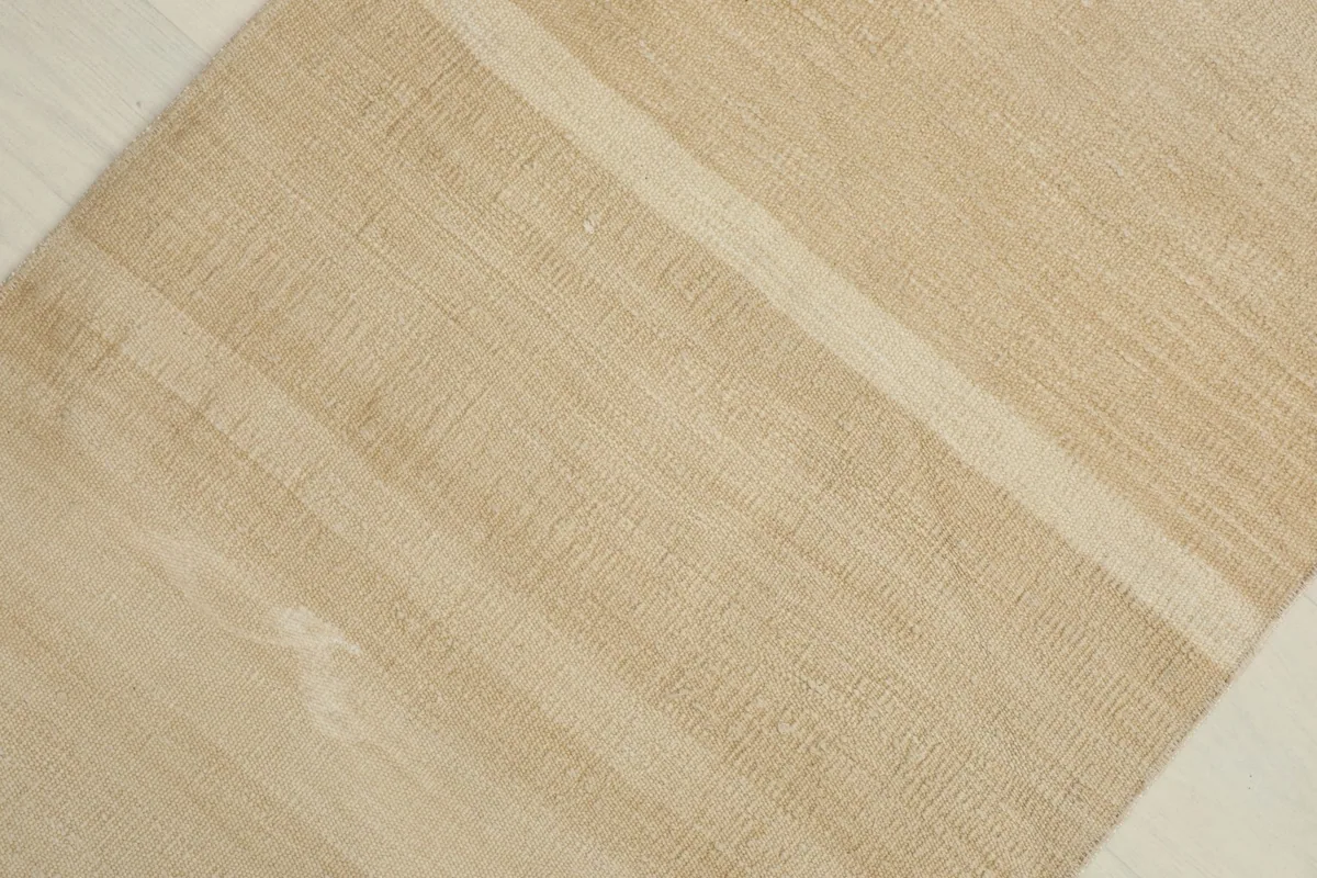 Angled view highlighting the natural beige and tan tones and the woven texture of the vintage rug.