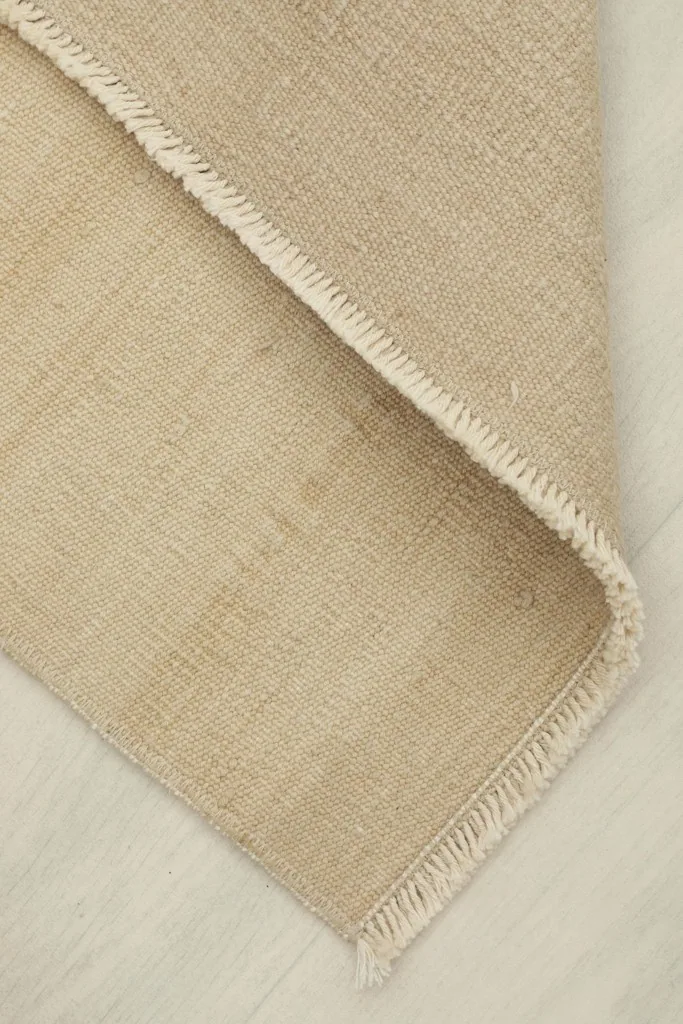 Corner of the rug folded back, showing the thickness and flexibility of the vintage wool material.