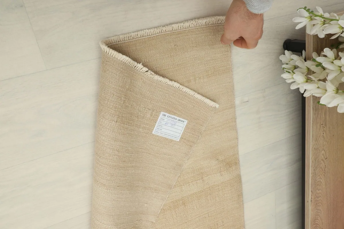 A hand rolling the rug, revealing the back and a label, demonstrating its handling and authenticity.