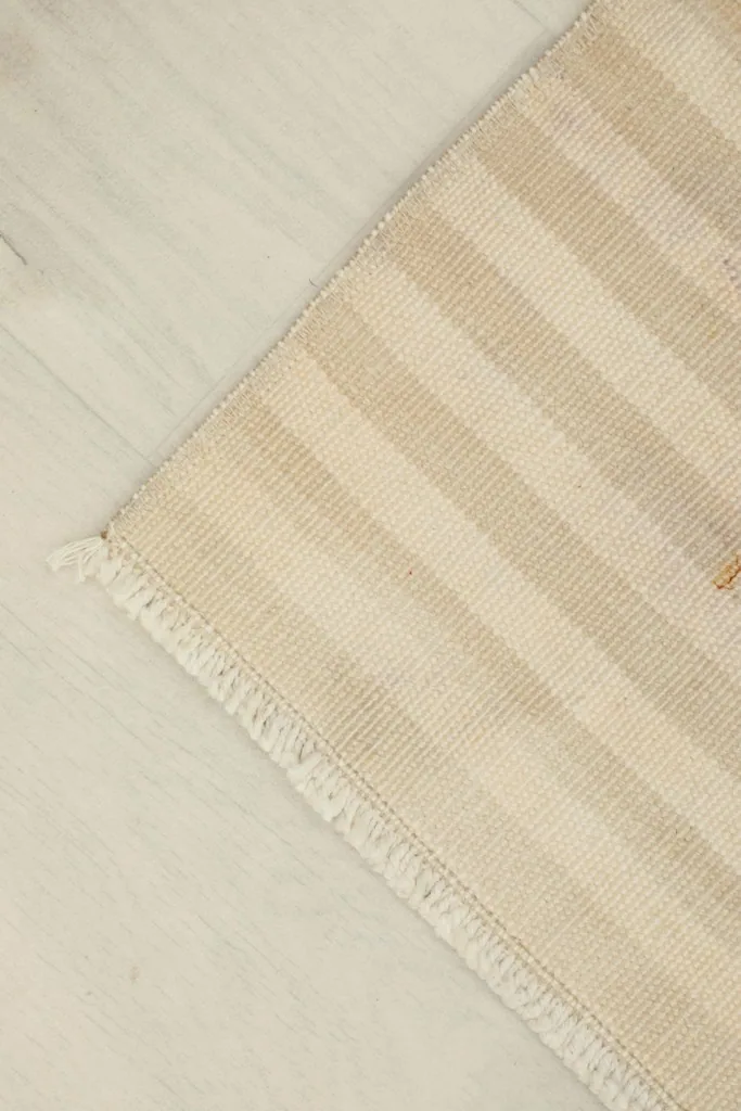 Corner view of the cream striped rug, illustrating its low pile and hand-knotted texture.
