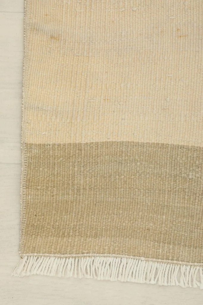 Edge view of the rug, focusing on the clean lines where the ivory meets the tan stripe and the short fringe.