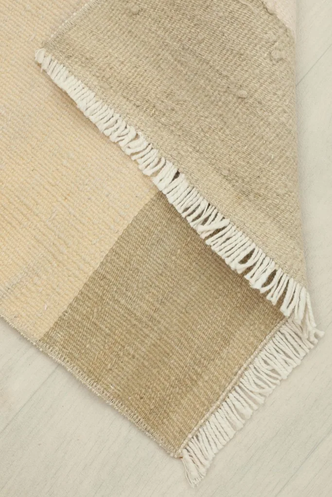 View of the rug with a corner folded over, revealing the cotton foundation underneath the wool pile.