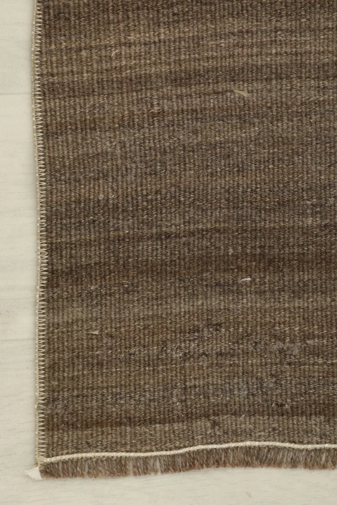 Close-up detail of the brown wool pile and hand-knotted texture of the vintage rug.
