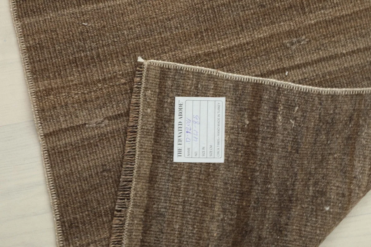 View of the back of the brown vintage doormat, showing the knotting and a product label.
