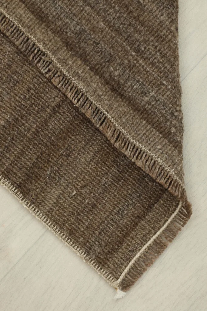Folded corner of the brown rug, revealing the thickness of the wool pile and cotton foundation.