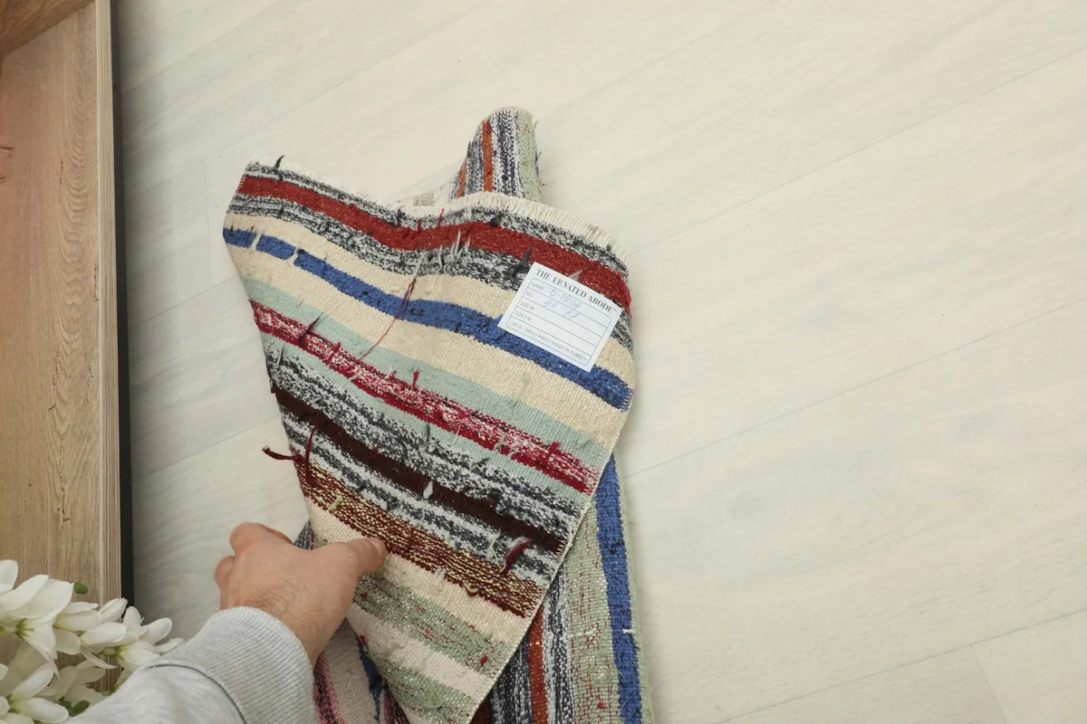 Hand holding the rug to show the reverse side and the hand-knotted construction.
