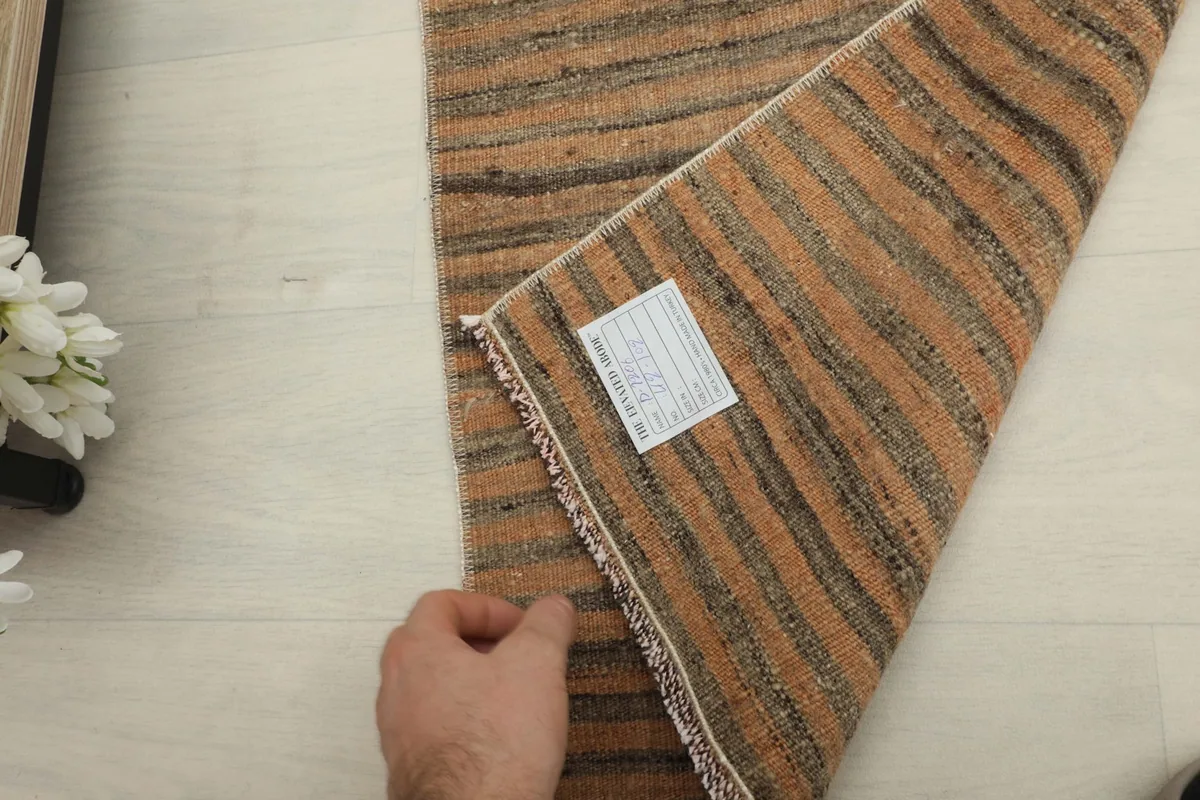 Hand holding back the rug to show the woven reverse side and a care label.