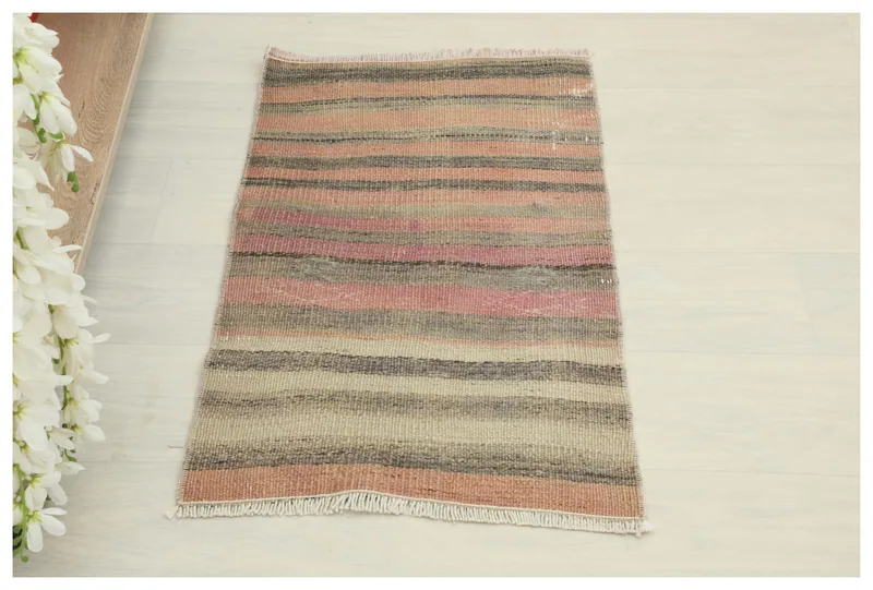Full overhead view of the rose, gray, and beige striped vintage Anatolian doormat on a white background.