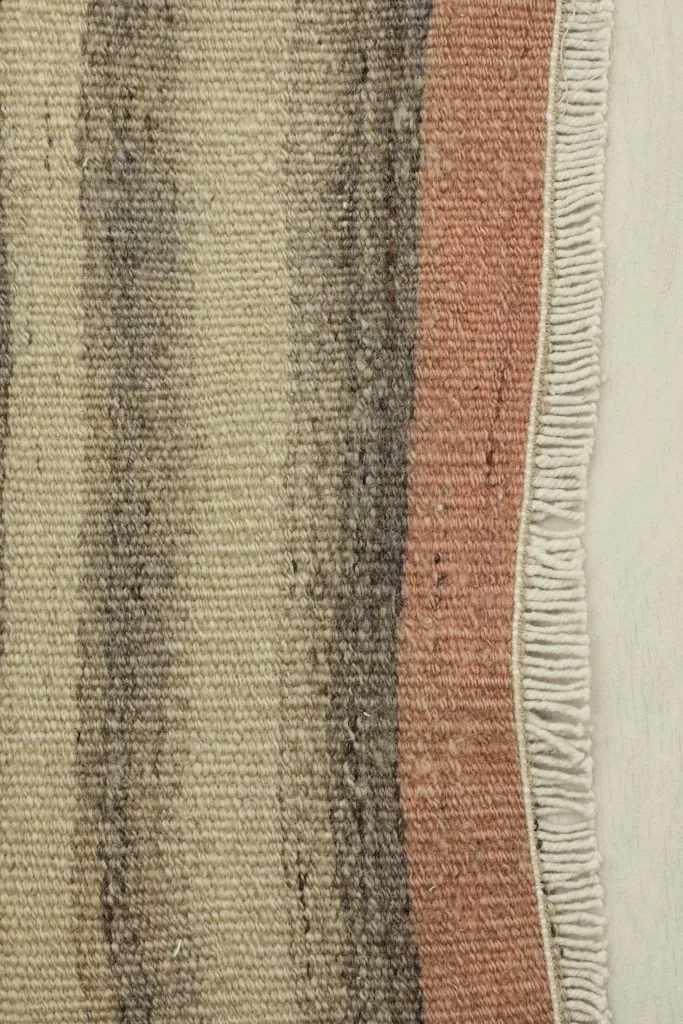 Close-up detail of the doormat's fringe and the distinct rose and gray stripes.