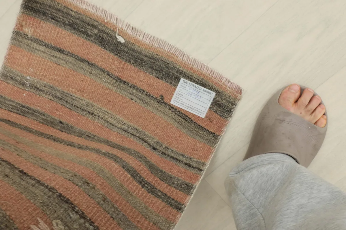 Overhead view of the doormat next to a foot for scale, showing the tag on the back.