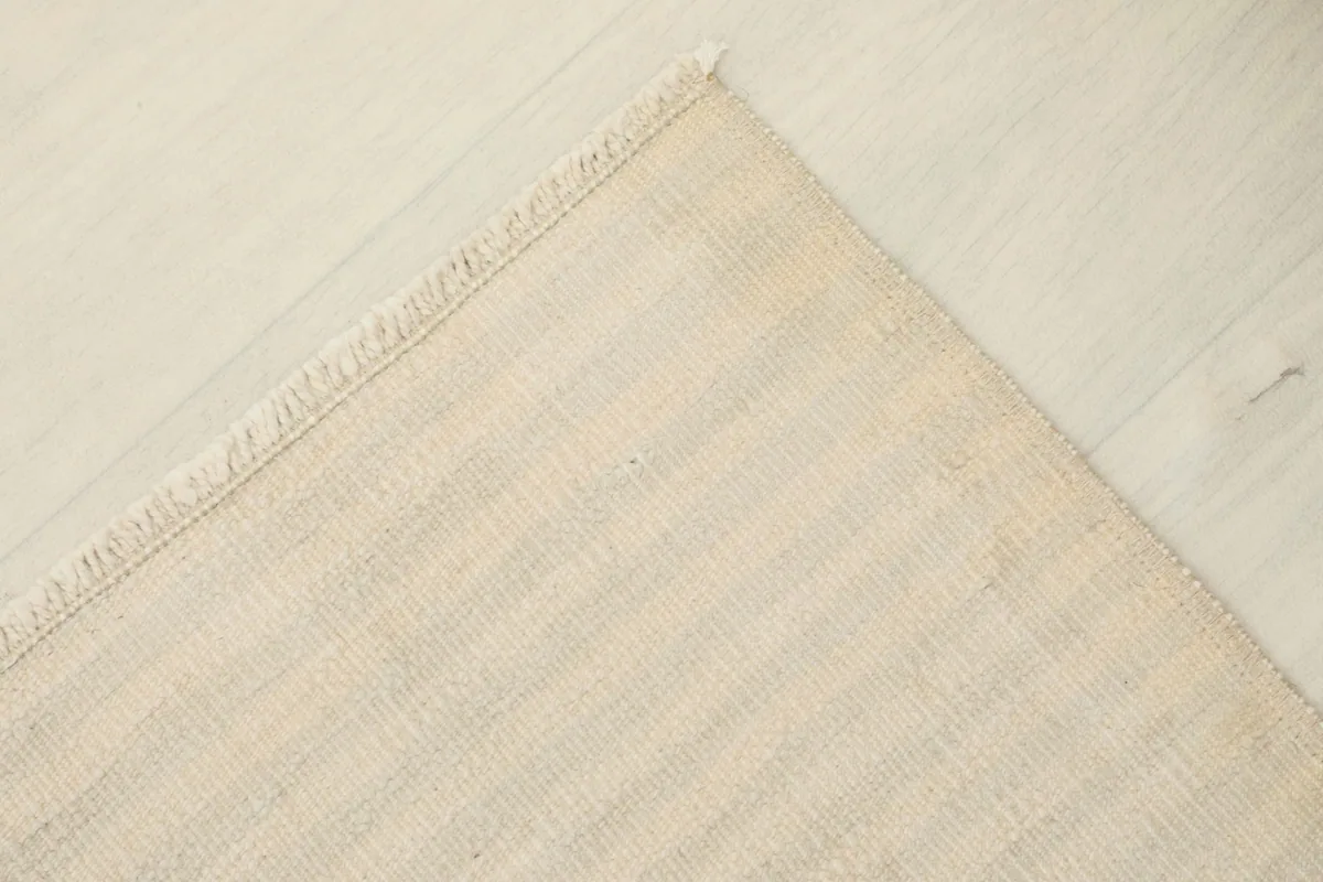 Corner view of the rug, displaying the tight weave and the natural undyed wool fibers.