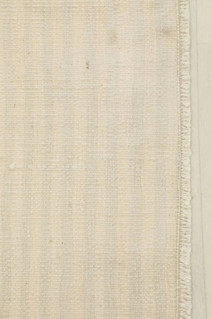 Close-up of the natural beige wool pile and the hand-knotted texture of the rug surface.